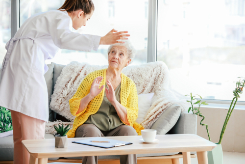 Female caregiver appearing to yell at an elderly woman sitting on a couch, illustrating potential elder abuse or mistreatment in a caregiving setting.